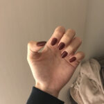 女性の左手、濃い紫のネイルを見せているシーン
