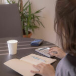 部屋で計算機を片手にノートをつけている女性