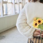 ひまわりを後ろ手に持つ女性